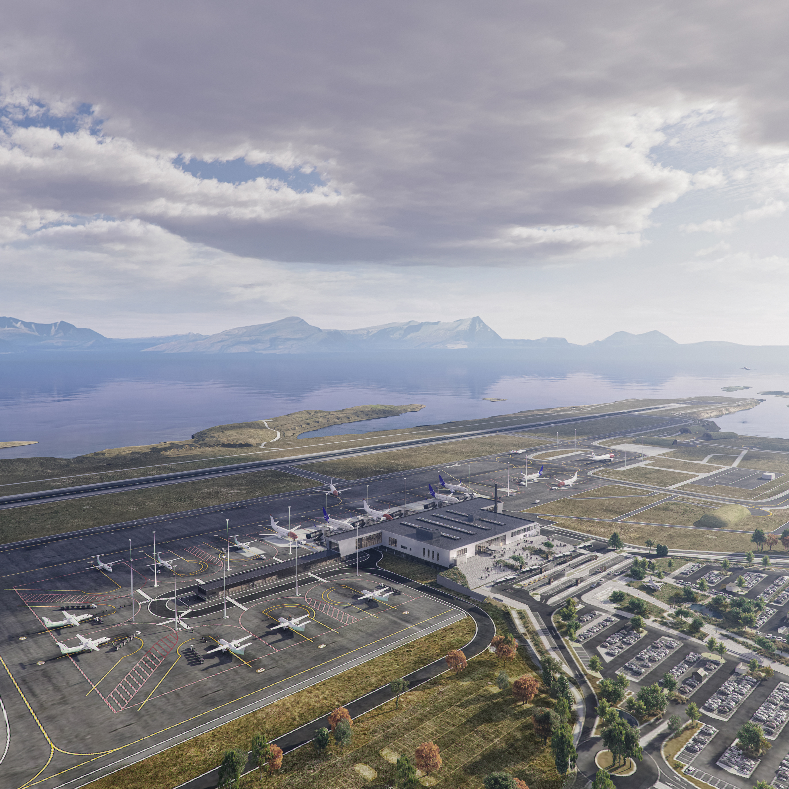 Aerial view of a coastal airport with planes on the tarmac, surrounded by parking lots and roadways, set against a backdrop of mountains and a body of water under a cloudy sky