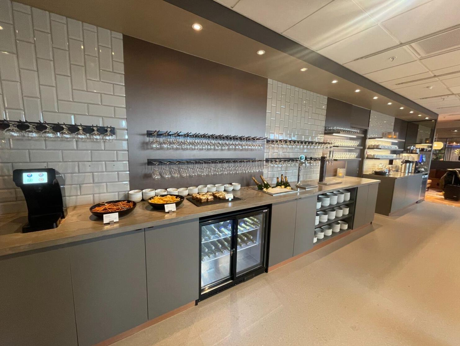 Modern buffet setup in a lounge with beverage dispensers, various appetizers, hanging glasses, and arranged plates, enhancing the dining experience