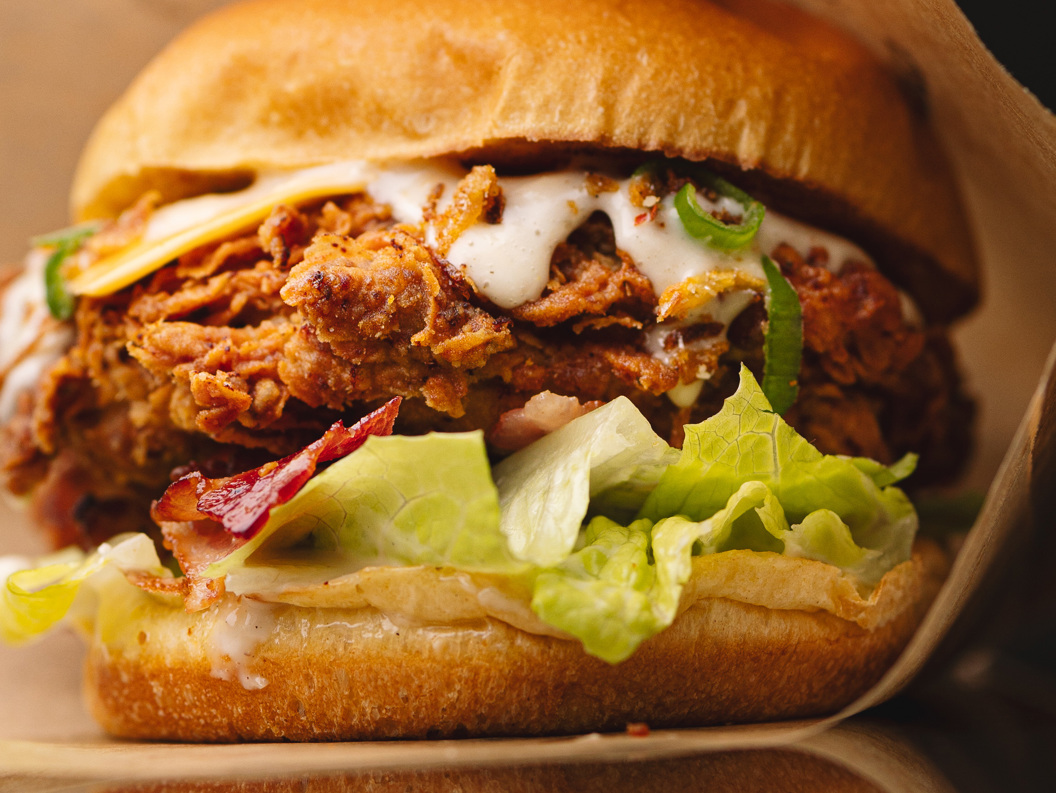 Close-up of a crispy fried chicken sandwich with lettuce, bacon, and creamy sauce on a toasted bun