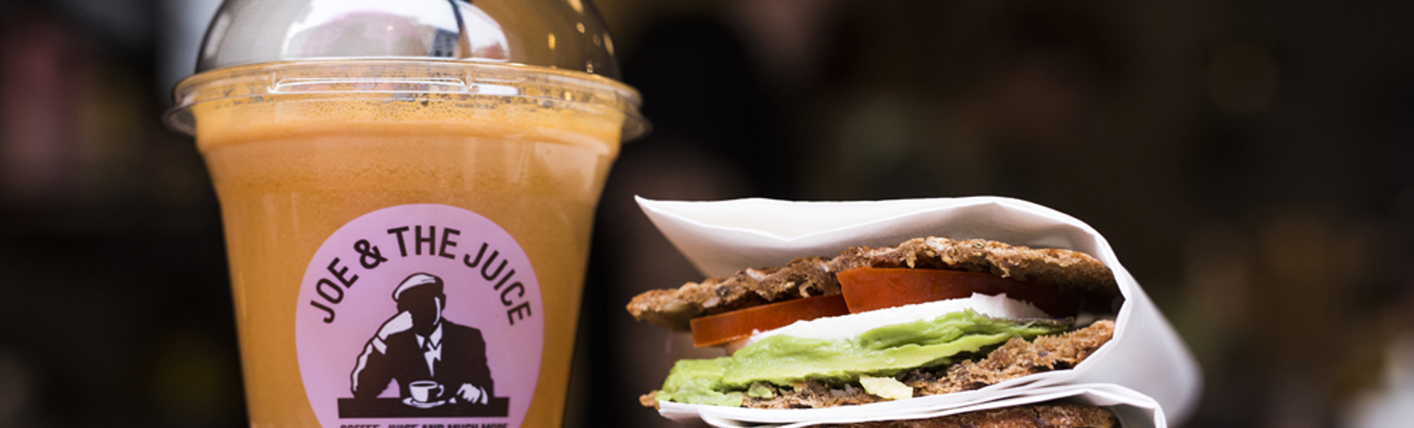 Kaldpressa juice frå "Joe & The Juice" ved sidan av ein sunn sandwich med avokado, tomat og mozzarella i brød servert på kafé