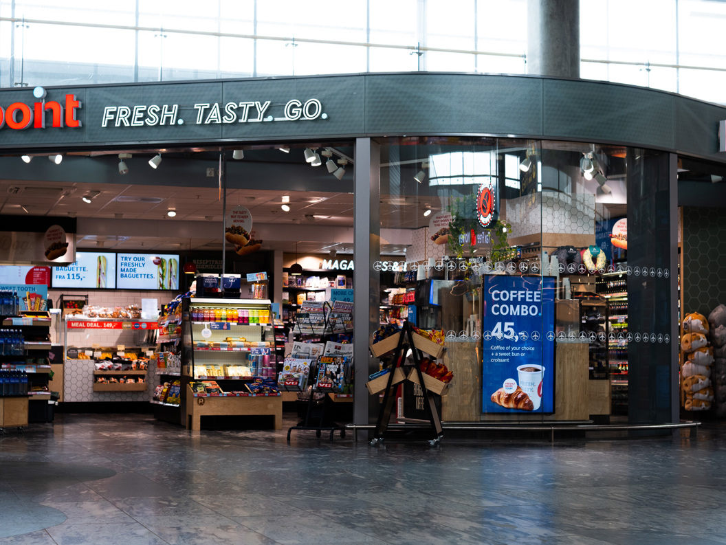 Butikkfasade av ein kiosk ved namn Point på ein flyplass, med stort utval av snacks, drikke og magasin synleg gjennom glasvindauget