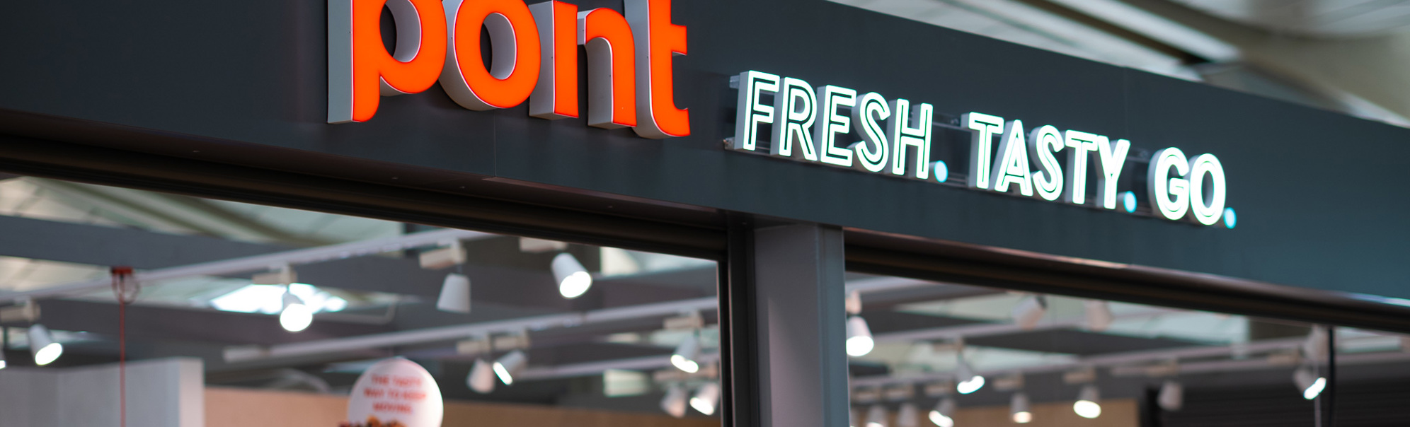 Butikkskilt med teksten "point" og slagordet "FRESH. TASTY. GO." i ein flyplassbutikk