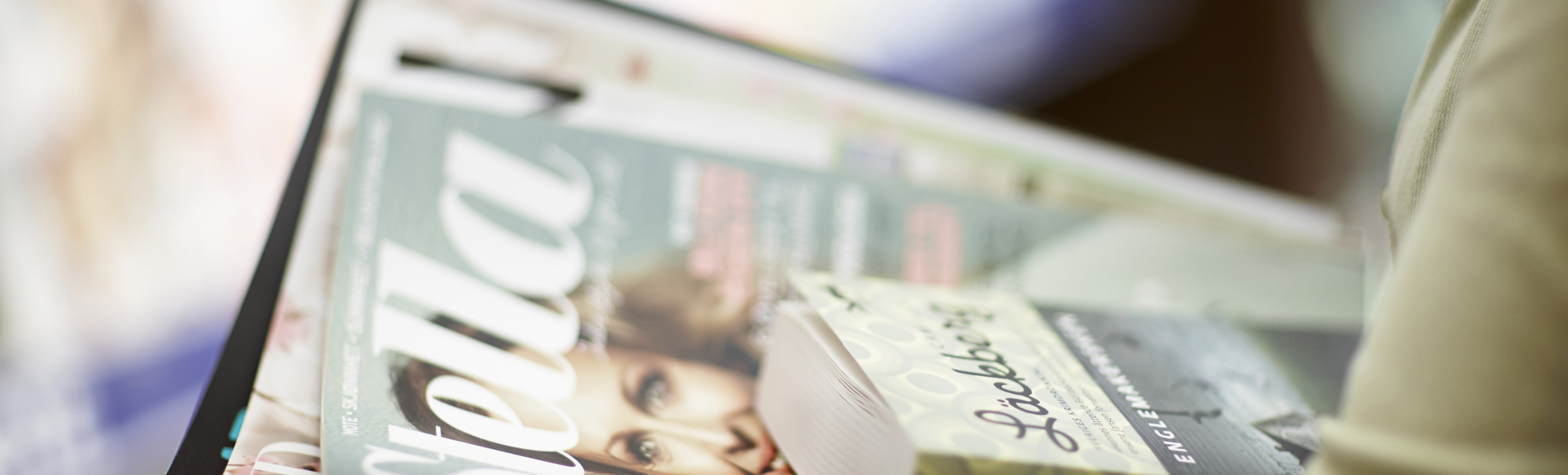 Person holding a stack of magazines and a book in a store, with the top magazine titled "Stella" and the book featuring an author's name