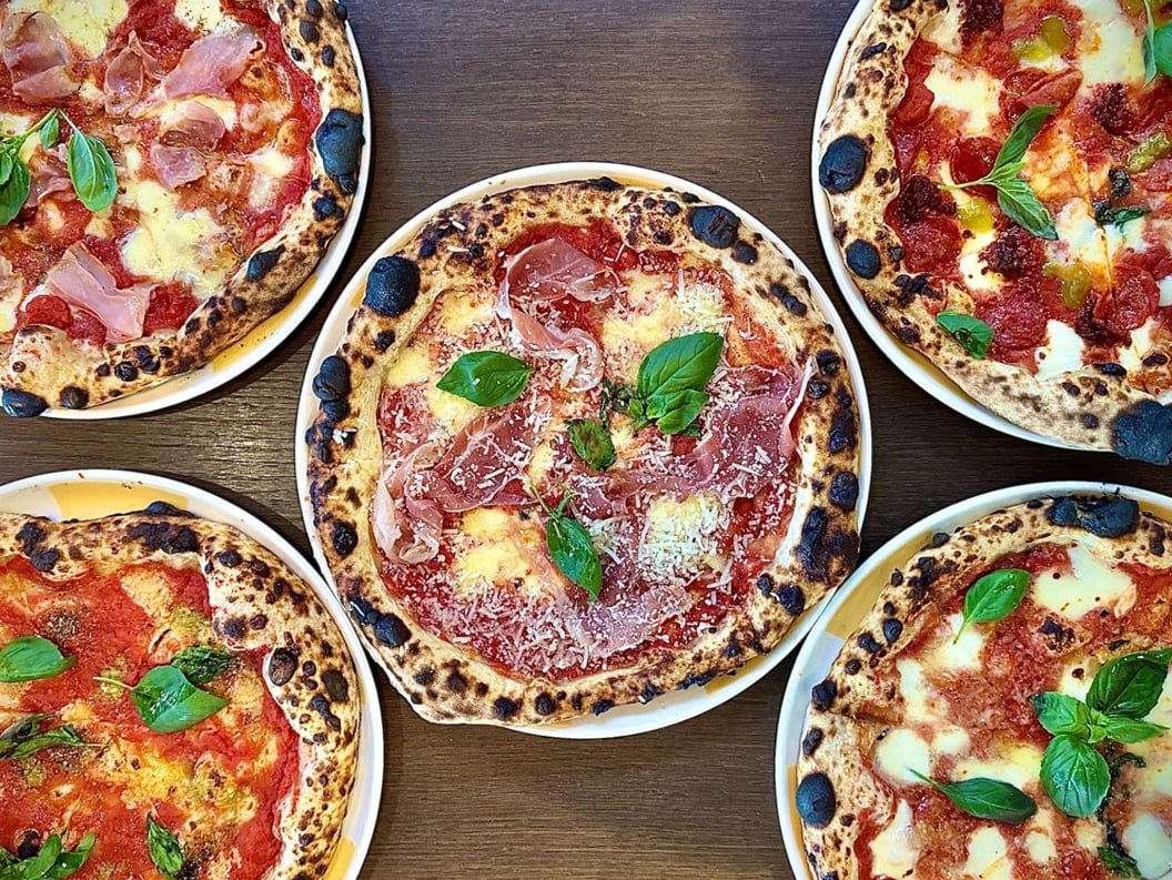 Fem håndverks-pizzaer med ulike toppinger inkludert basilikum, ost og spekemat på et trebord