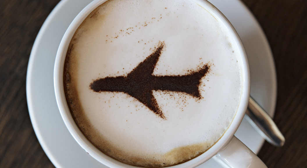 Cappuccino with airplane design in cinnamon on frothy milk, served in a white cup and saucer on a wooden table