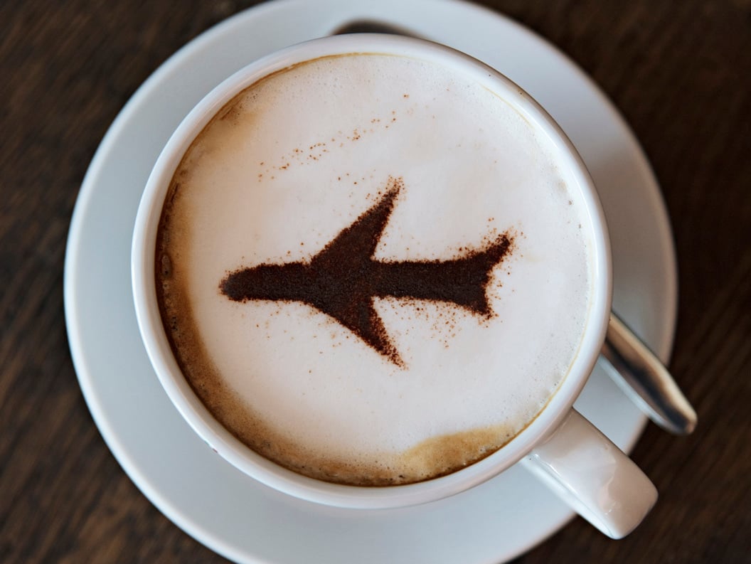Cappuccino med flydesign i kanel på skummet melk, servert i en hvit kopp og skål på et trebord