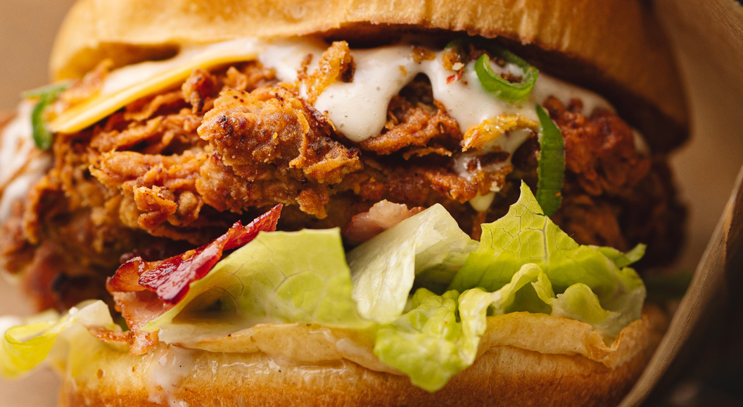 Crispy fried chicken sandwich with lettuce, bacon, cheese, and creamy sauce in a brioche bun