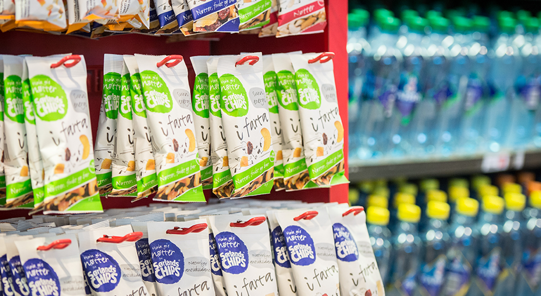 Snackposer på en rød butikkhylle, ved siden av en kjøler med flaskevann i en butikkomgivelse
