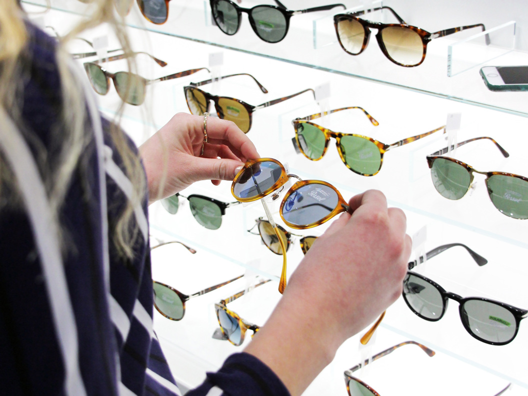 Kunde ser på briller i optikerbutikk, utstilling med ulike solbriller