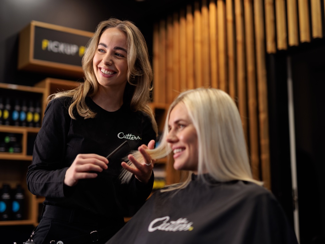 Frisør smiler medan ho friserer ein kunde med langt blondt hår i ein moderne frisørsalong