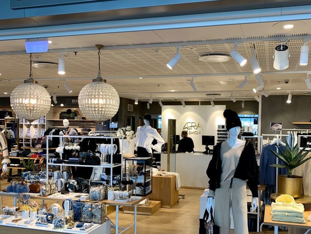 Motebutikk med namnet ÆRA, viste eit elegant interiør med klede, tilbehør og dekor på utstilling. Moderne lysdesign og velordna butikkmiljø
