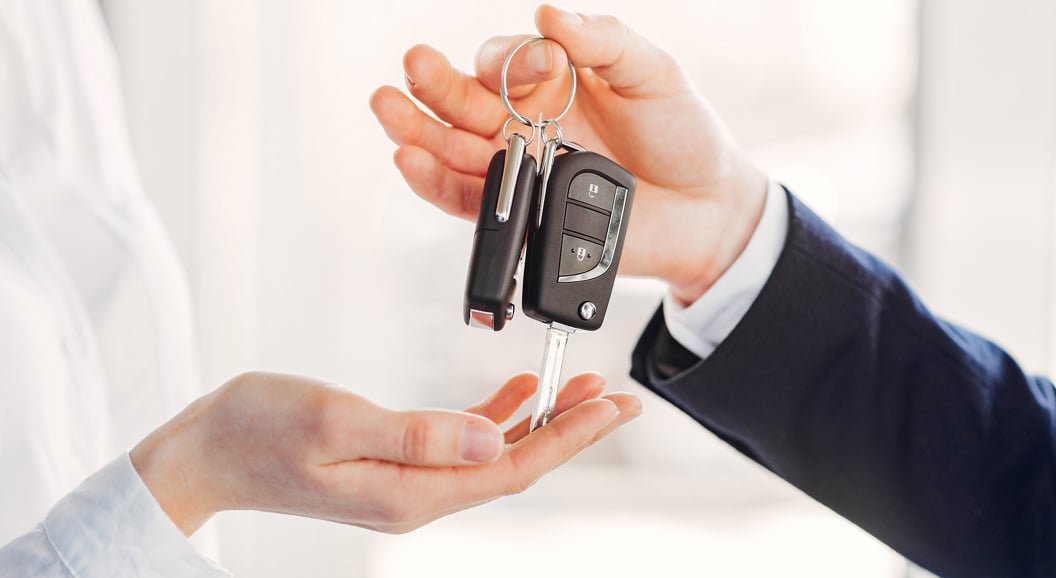 Person handing over car keys in a professional setting, symbolizing a car purchase or rental transaction
