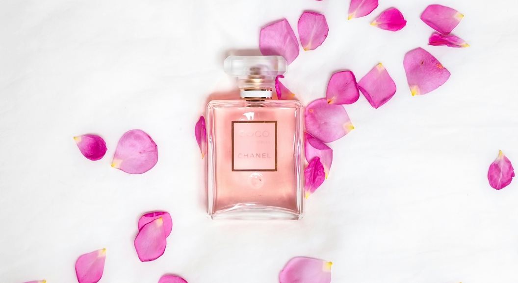 Pink perfume bottle surrounded by pink rose petals on a white background, creating an elegant and feminine aesthetic