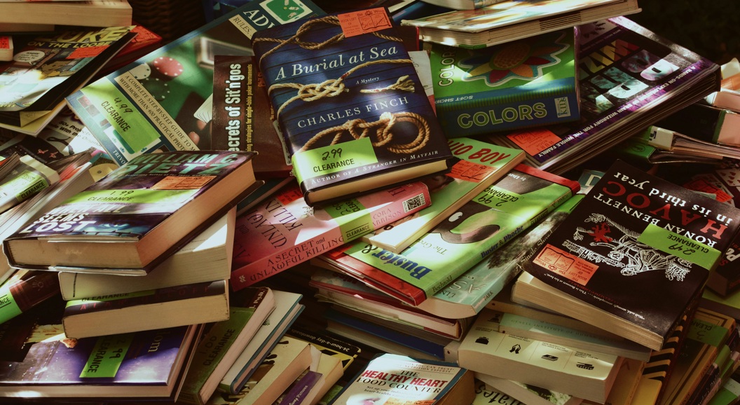 Pile of assorted books with colorful covers on a clearance sale table, featuring various genres and titles