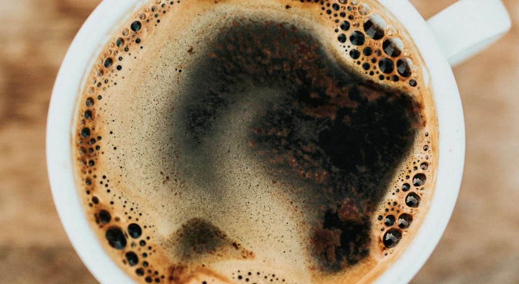 Cup of black coffee with frothy surface on a wooden table background