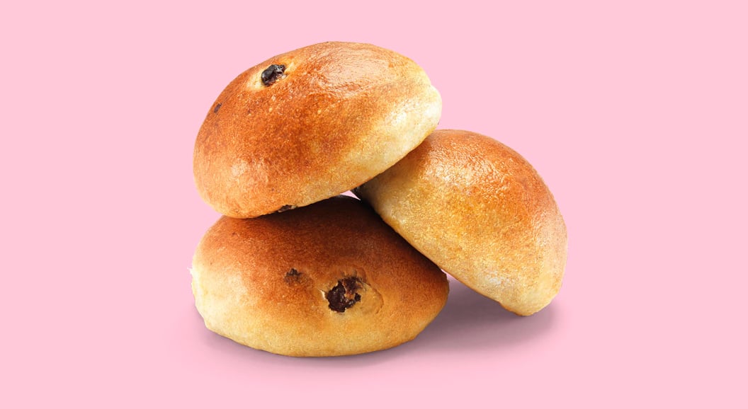 Tre rosinboller stablet på rosa bakgrunn.