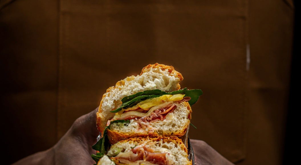 Håndlaget sandwich med ferske ingredienser holdt i hender iført et brunt forkle
