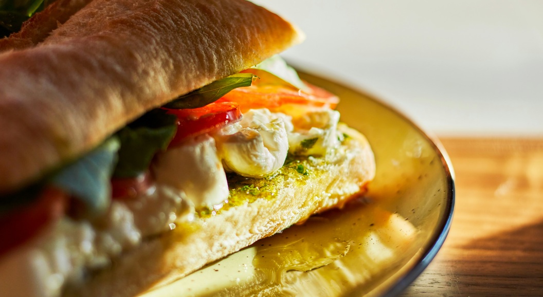 Fresh mozzarella and tomato sandwich with basil and pesto on a yellow plate, bathed in warm sunlight