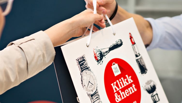 Person receiving a shopping bag with "Klikk & hent" text, featuring images of a watch and lipstick, symbolizing tax-free shopping and convenience