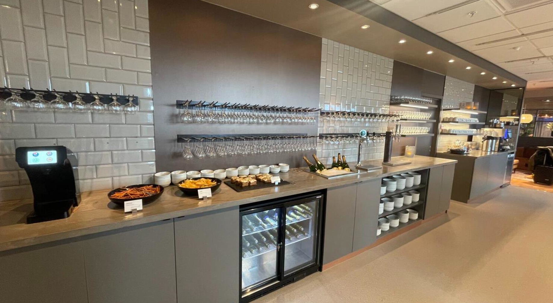 Moderne buffetoppsett i en lounge med drikkedispenser, ulike forretter, hengende glass, og arrangerte tallerkener, som forbedrer spiseopplevelsen