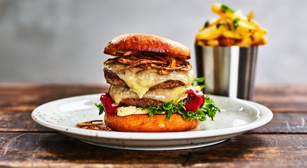 Gourmet cheeseburger med sprøstekt løk, salat og tomater på en ristet bolle, servert med en side av gyldne pommes frites i en metallkopp