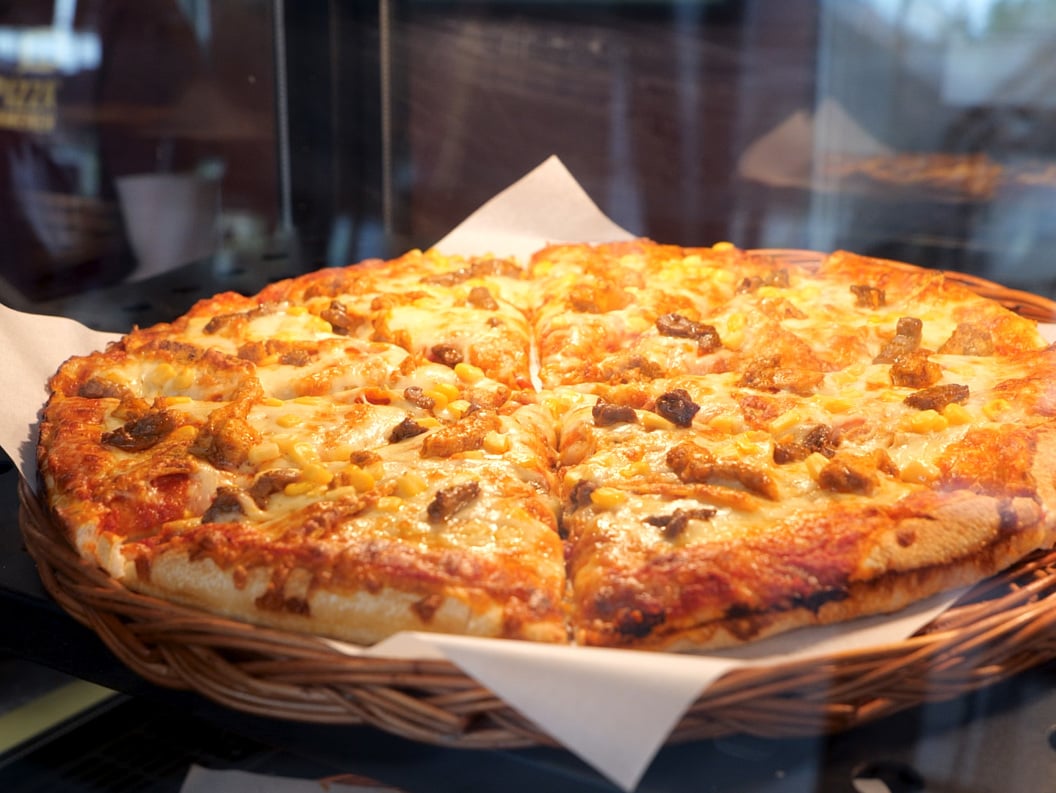 Nystekt pizza med ostetopping og sopp, presentert i en kurvkurv på bakepapir