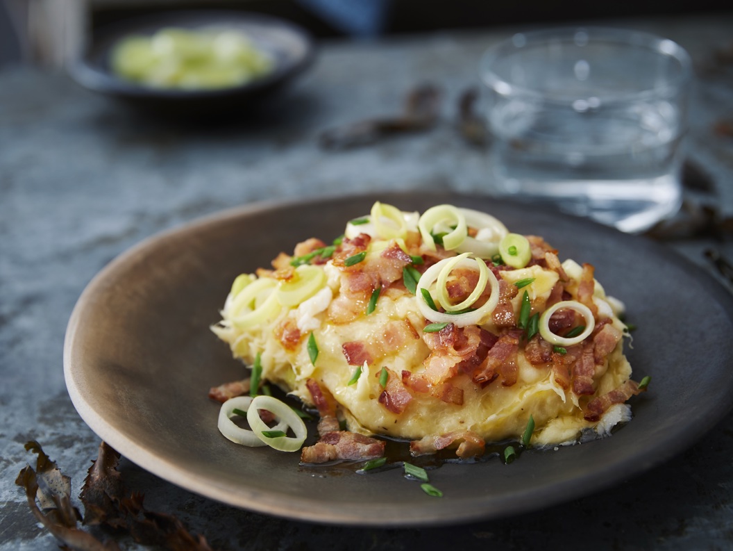 Kremet potetgrateng toppet med sprø bacon og fersk vårløk, servert på en rustikk keramikkfat