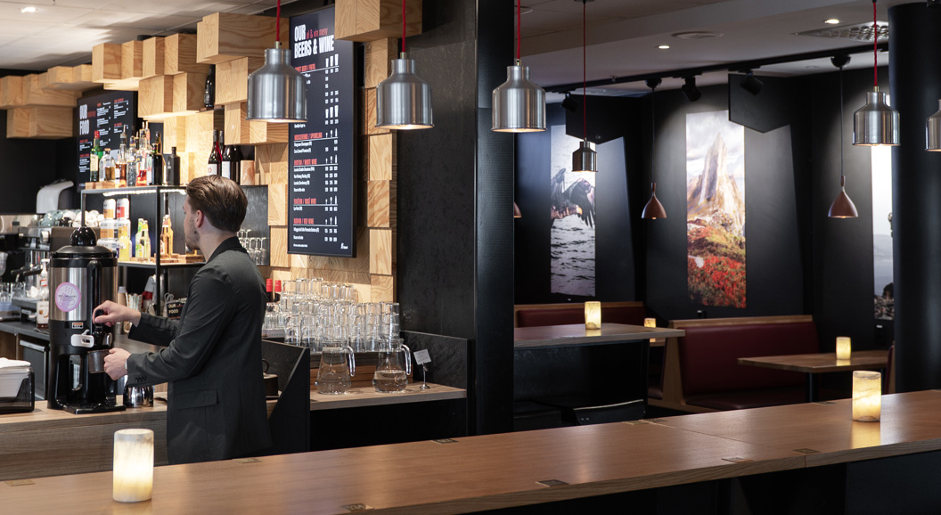 Kafeteria med moderne interiør, sitjeplassar, kunst på veggane og ein tilsett som lagar kaffi bak disken