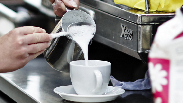 Barista pouring steamed milk into a coffee cup, creating latte art in a cafe setting