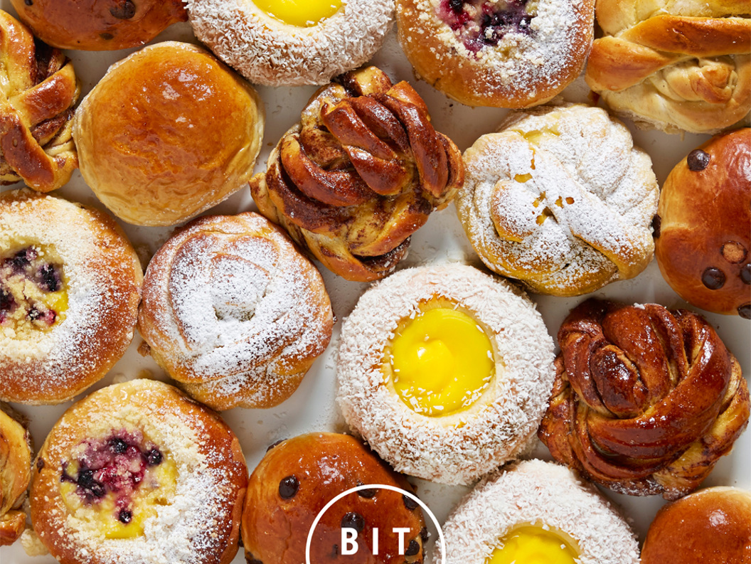 Assorted pastries featuring Danish pastries, buns, and sweet rolls with fruit and custard fillings, topped with powdered sugar, and branded with "BIT UNION" logo