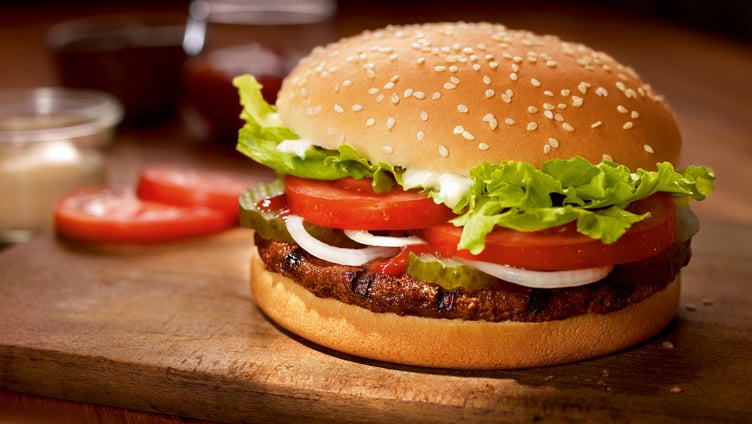 Delicious burger with beef patty, fresh lettuce, tomato slices, onions, pickles, and sesame seed bun on wooden board