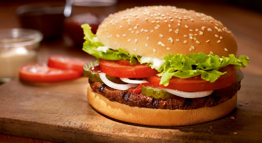 Delicious burger with beef patty, fresh lettuce, tomato slices, onions, pickles, and sesame seed bun on wooden board
