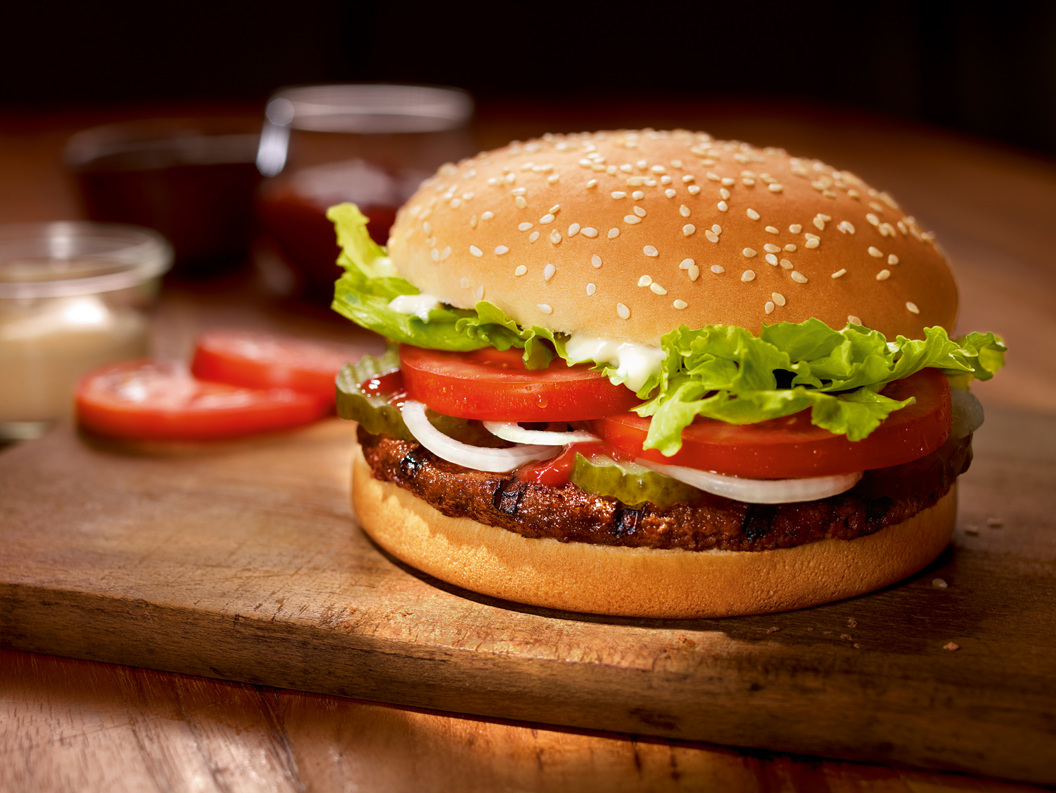 Saftig hamburger med salat, tomat, løk og sylteagurk på ein treplate