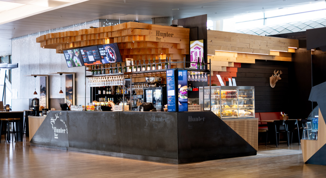 Moderne kafe med tresøyler og glasmonter, serverer drikke og snacks i ein flyplasslounge