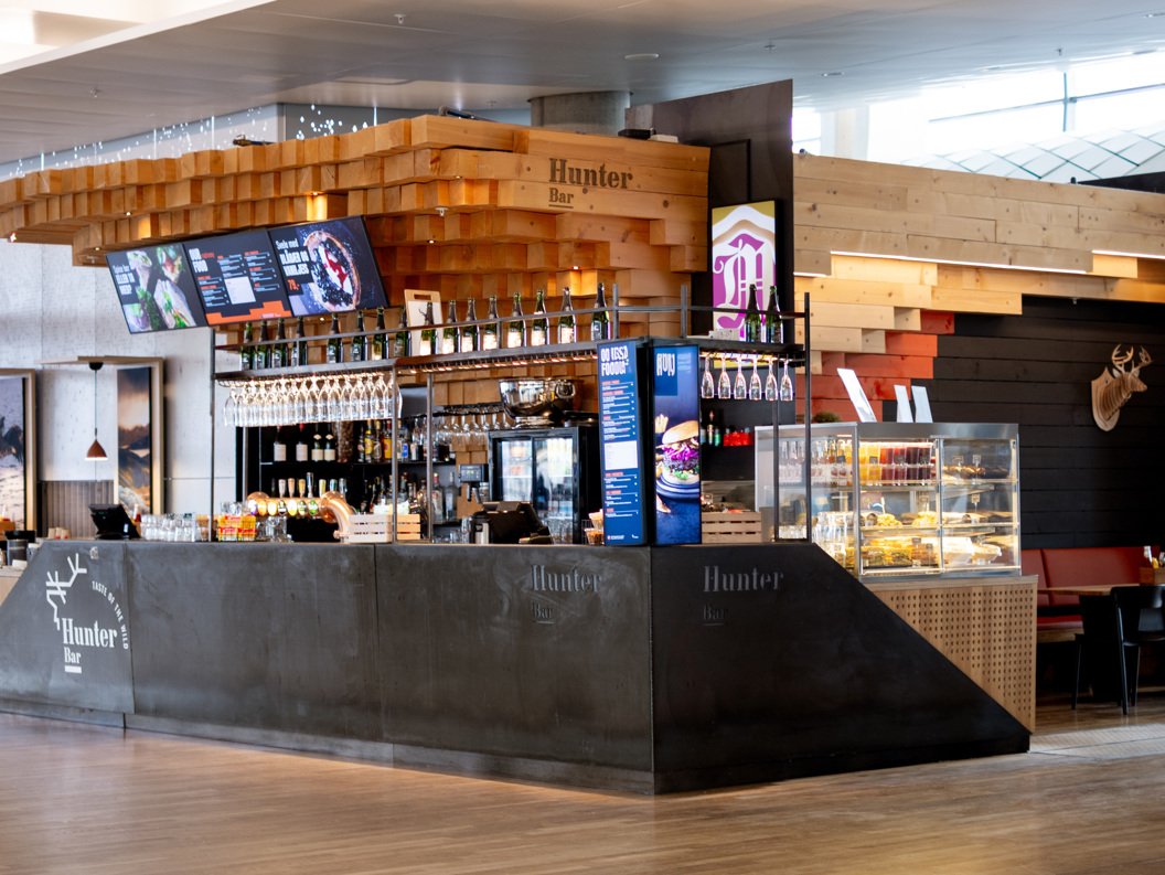 Modern bar interior with wood accents and sleek design at Hunter Bar, showcasing a digital menu, hanging glasses, and a display case with food items