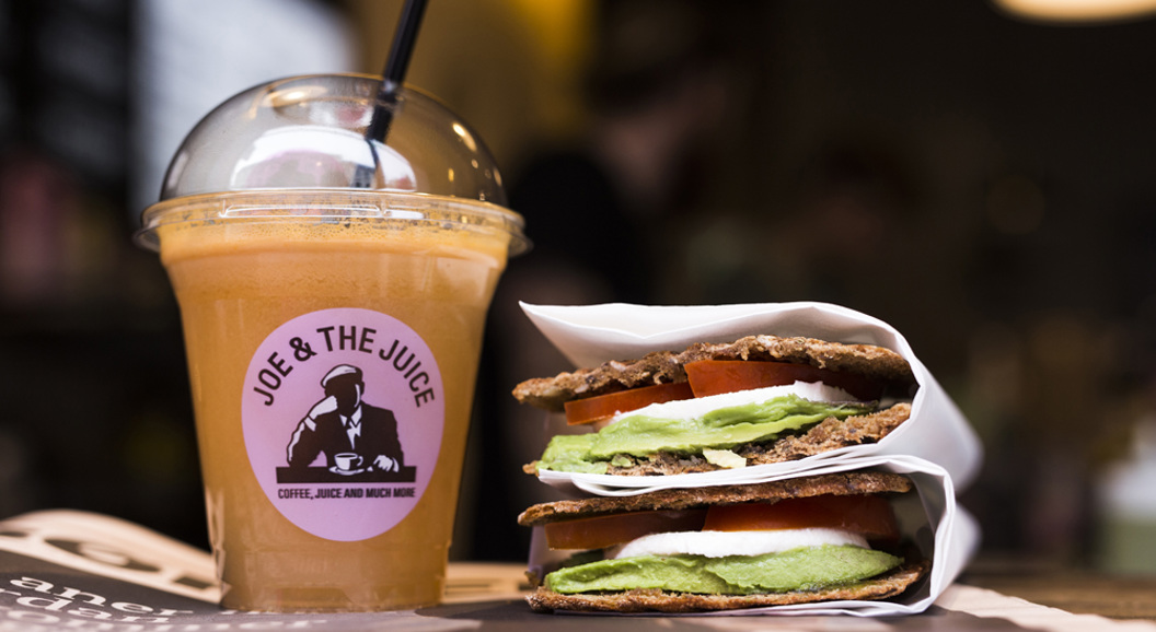 Kaldpressa juice frå "Joe & The Juice" ved sidan av ein sunn sandwich med avokado, tomat og mozzarella i brød servert på kafé