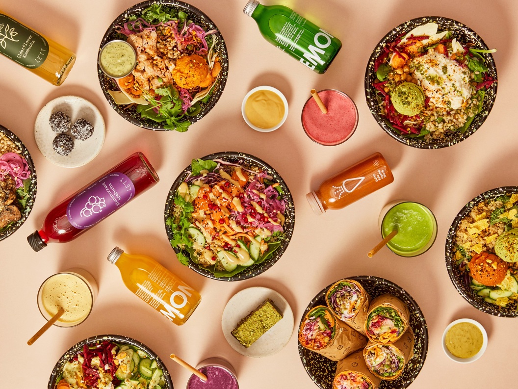 Fargerike salatskåler, wraps og smoothieflasker med ulike ingrediensar som grønsaker, frø og sausar, sett ovanfrå på ein lysebrun bakgrunn