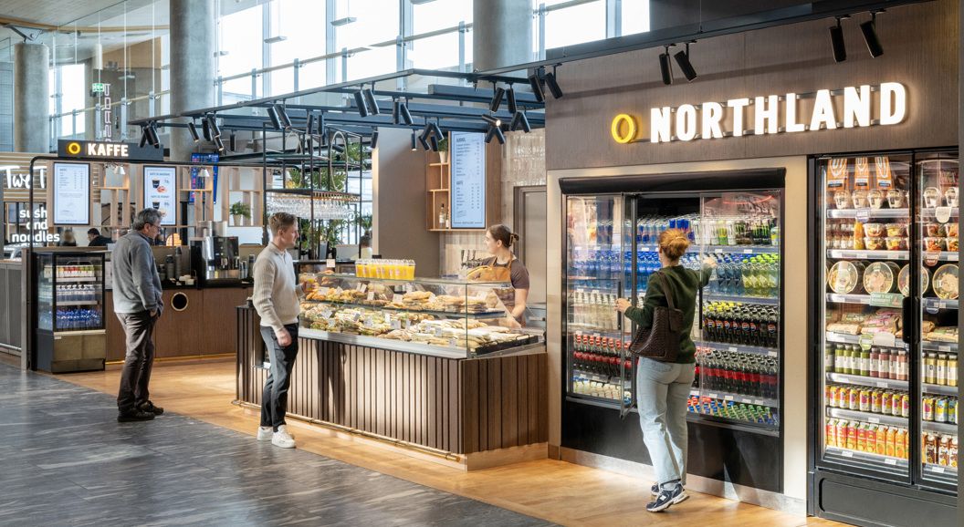 Kiosk i flyplass med folk som kjøper mat og drikke frå diskar og kjøleskap hjå Northland, moderne interiør i lyse omgjevnader