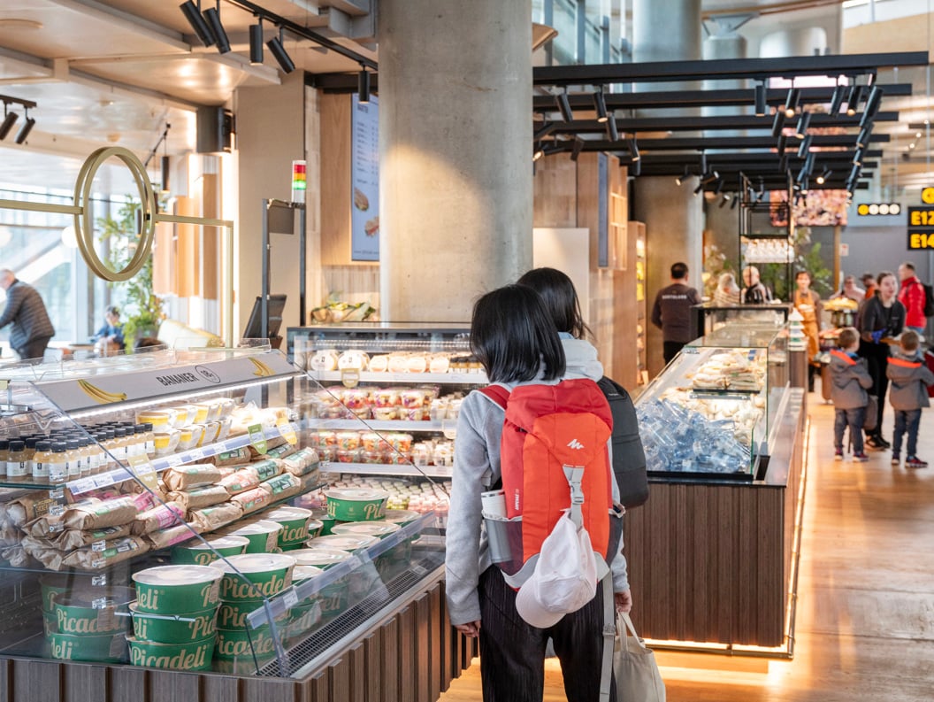 Folk som ser på matutvalg ved en moderne flyplassdelidisk med forskjellige pakkede varer og ferske produkter