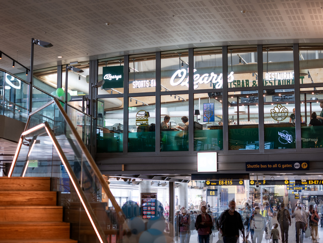 Restaurant O'Learys på ein flyplass med utsikt over reisande i terminalen, tretrapp i forgrunnen, oppe og innendørs atmosfære