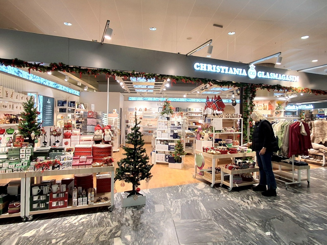 Butikken til Christiania Glasmagasin med et godt opplyst utstillingsvindu med smykker, klær og interiørartikler i et moderne kjøpesentermiljø