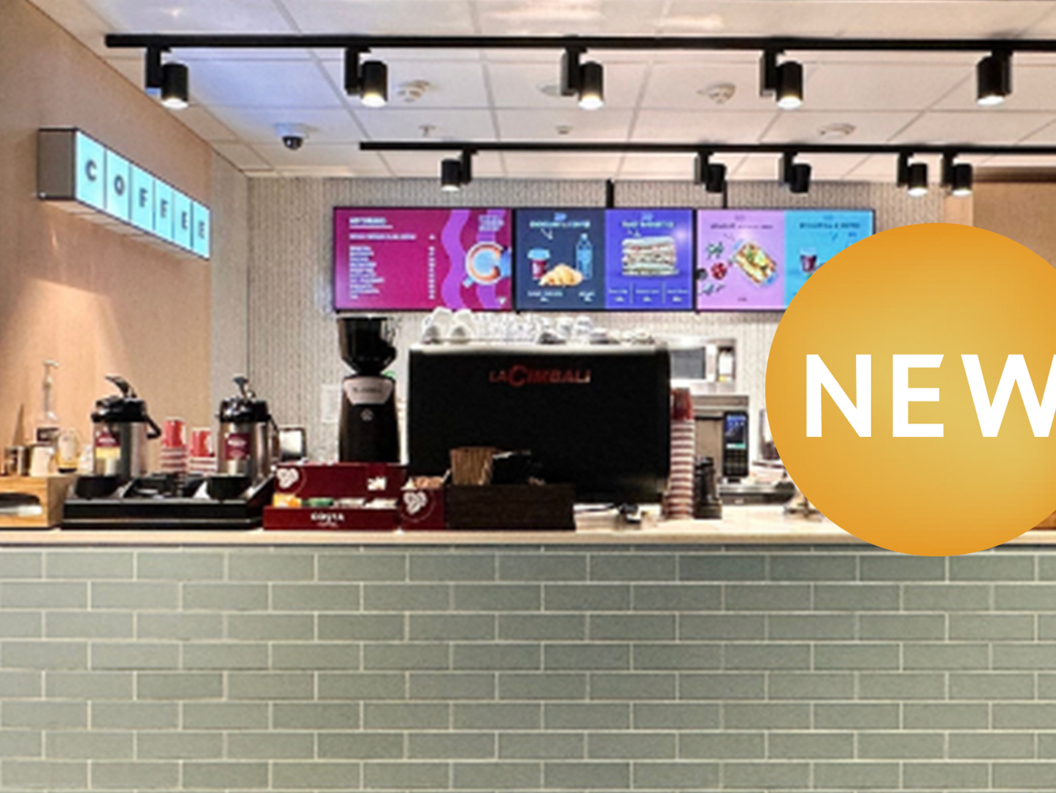 Modern coffee shop counter with a new menu displayed on digital screens, featuring an espresso machine and an assortment of coffee supplies