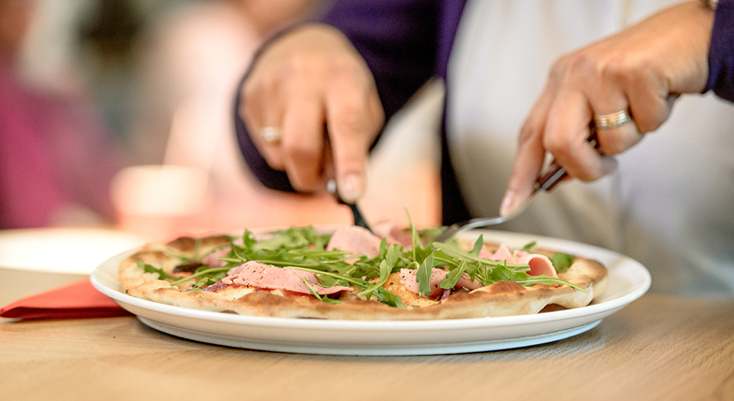 Person et pizza med ruccola og skinke med kniv og gaffel