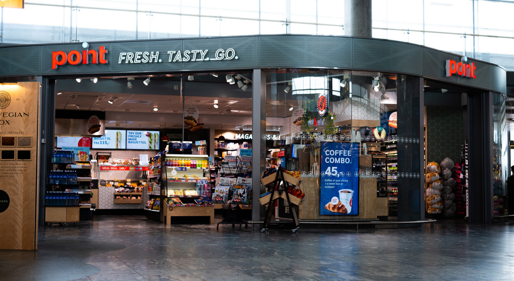 Butikkfasade av ein kiosk ved namn Point på ein flyplass, med stort utval av snacks, drikke og magasin synleg gjennom glasvindauget