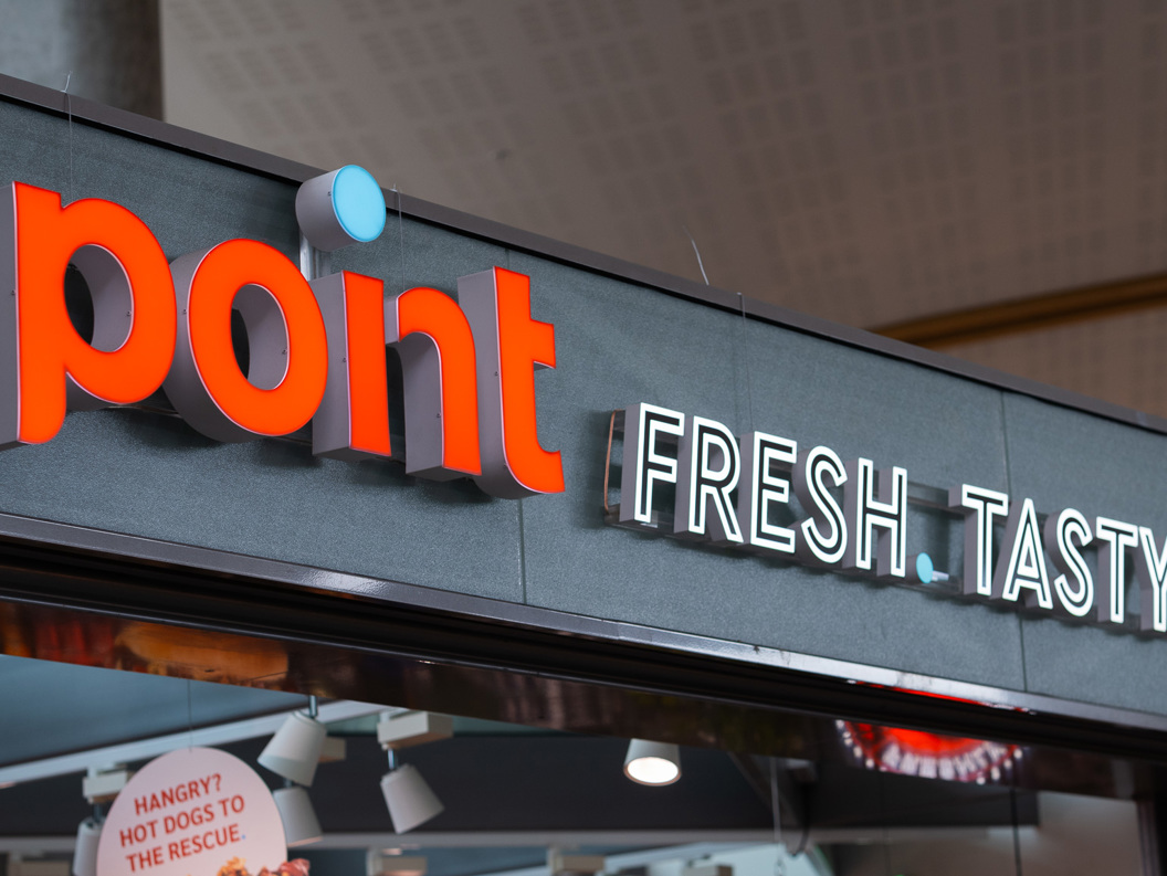 Skilt med teksten "Point Fresh Tasty Go" på ein kiosk i moderne design, inne i ein bygning