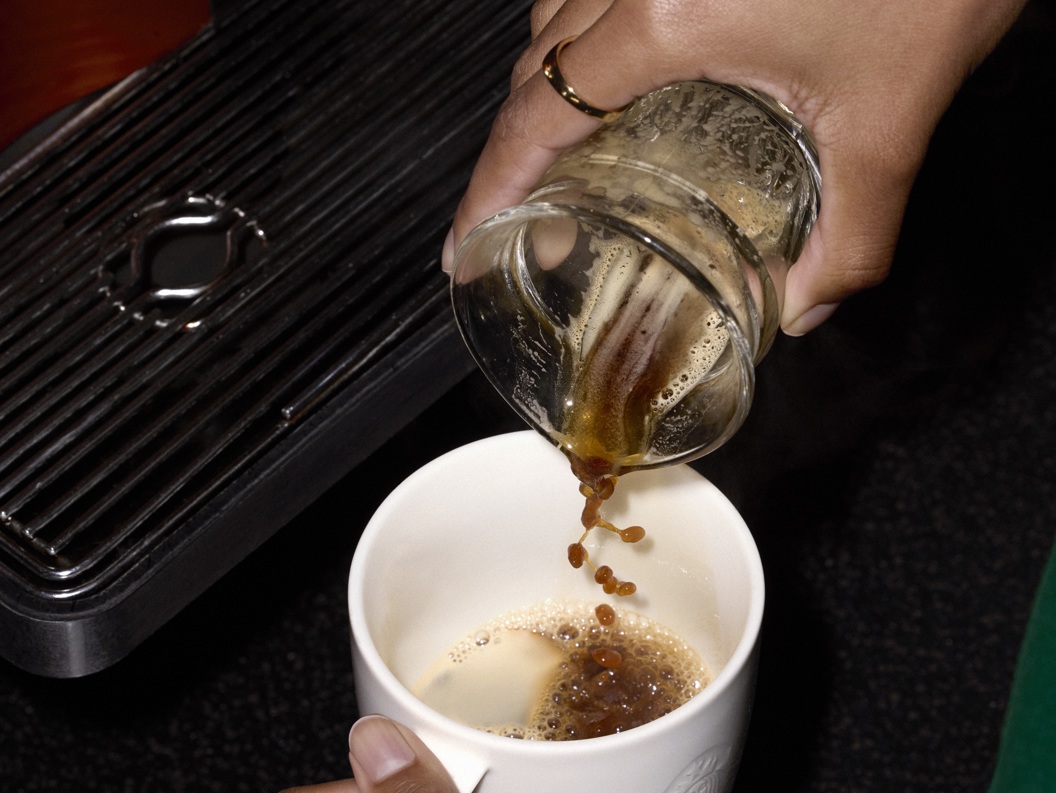 Person heller kaffe fra glass til kopp ved en kaffemaskin