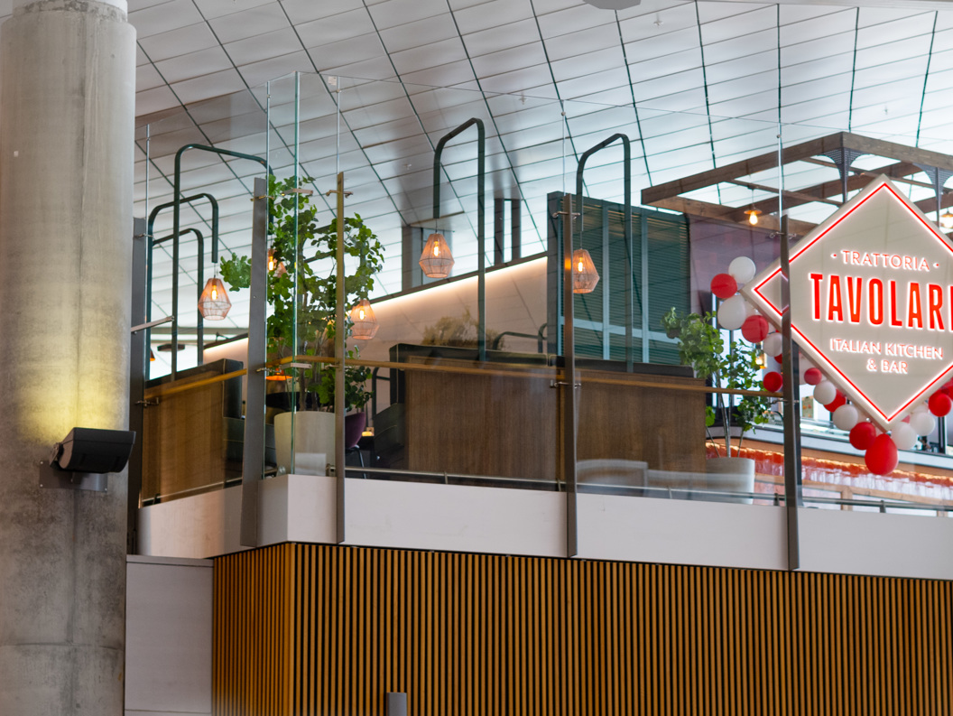 Tavolare Italian Kitchen & Bar sign within a modern shopping complex, featuring glass railings and decorative lighting