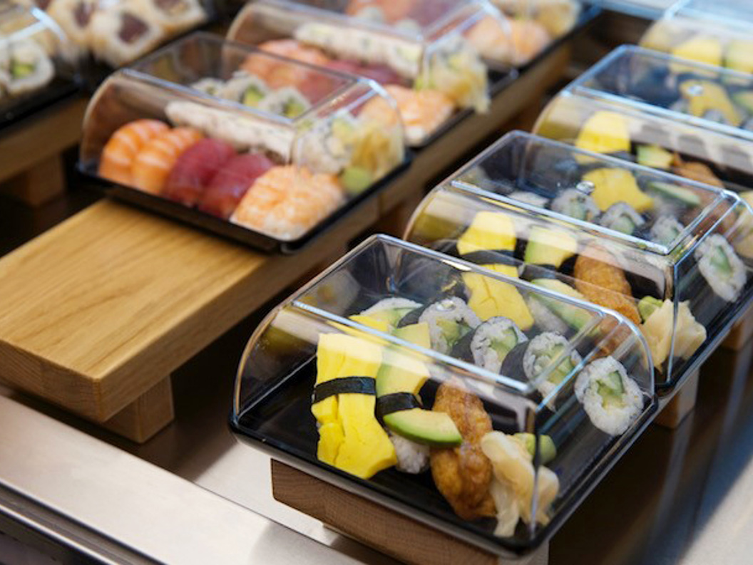 Assorterte sushifat i take-away beholdere med fersk nigiri og ruller, vist på en trebenk i en sushi restaurant