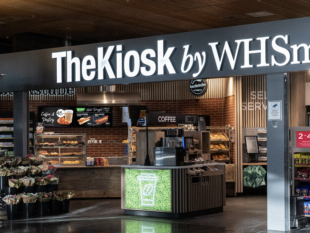 The Kiosk by WHSmith located in an indoor shopping area, featuring a selection of food, drinks, snacks, and magazines for sale