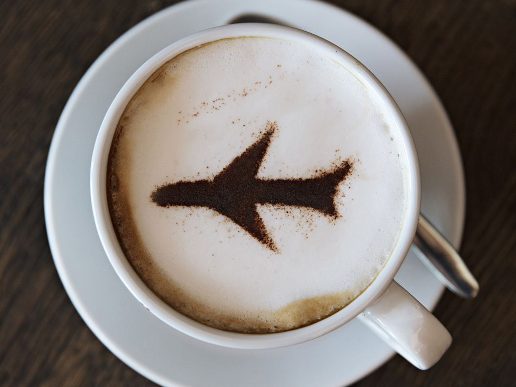 Cappuccino med flydesign i kanel på skummet melk, servert i en hvit kopp og skål på et trebord